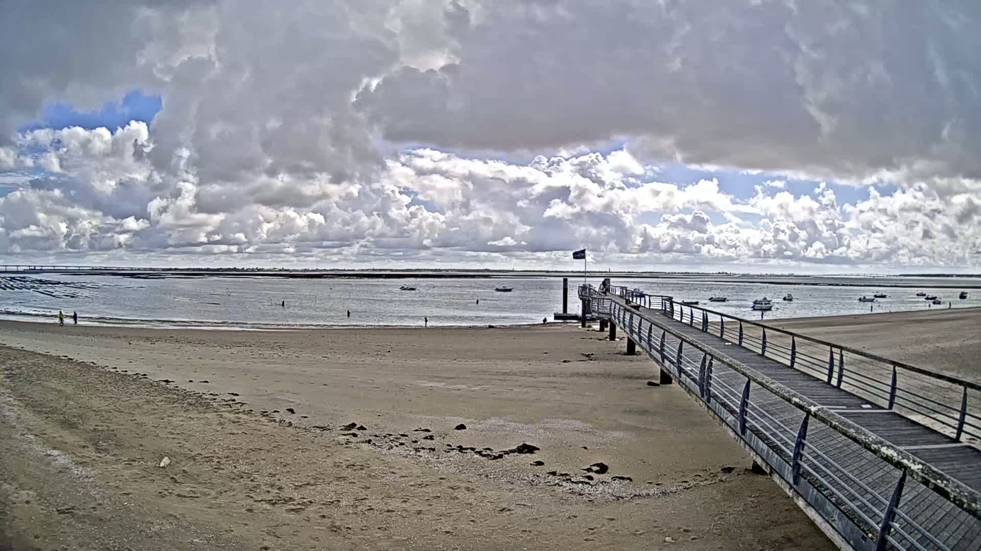 A long pier extends from a sandy beach toward a calm body of water under a partly cloudy sky.