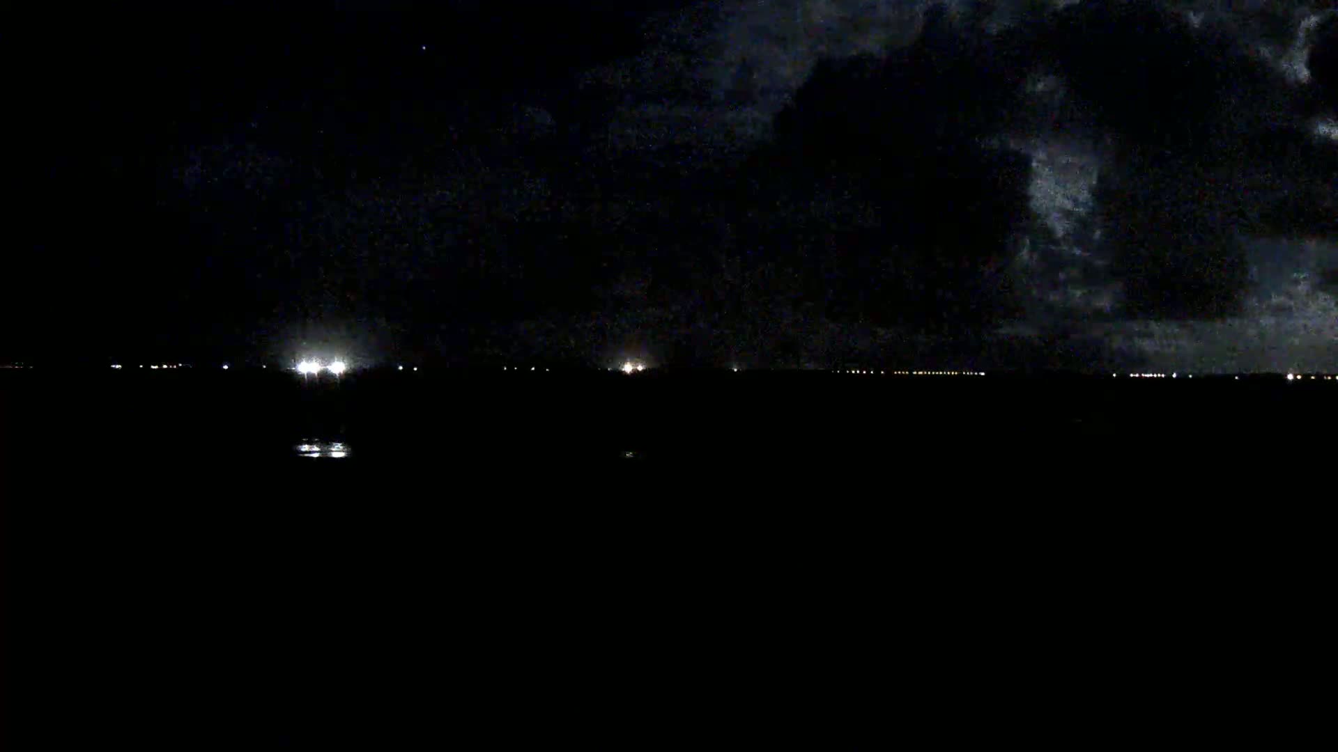 A dark, nighttime scene shows a distant line of lights under a cloudy sky.