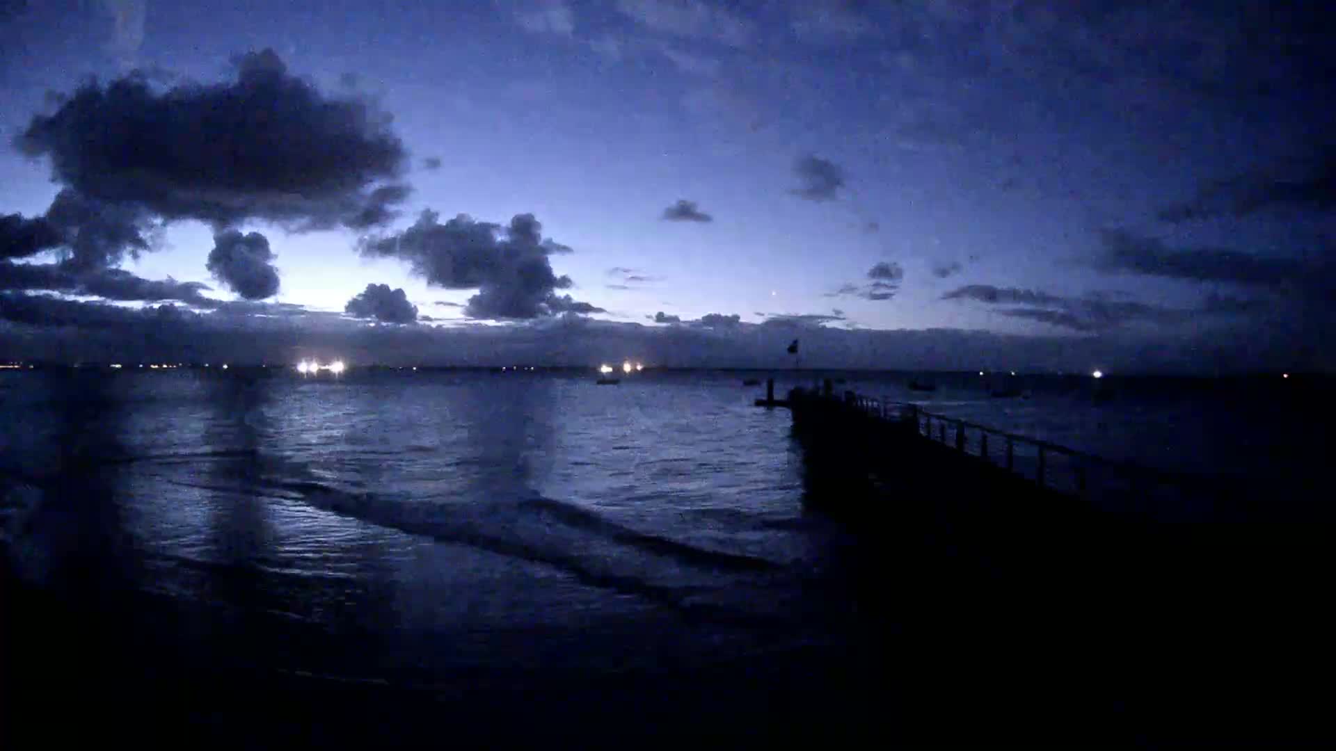 A dark, cloudy twilight sky overlooks a calm sea with a pier extending into the water.
