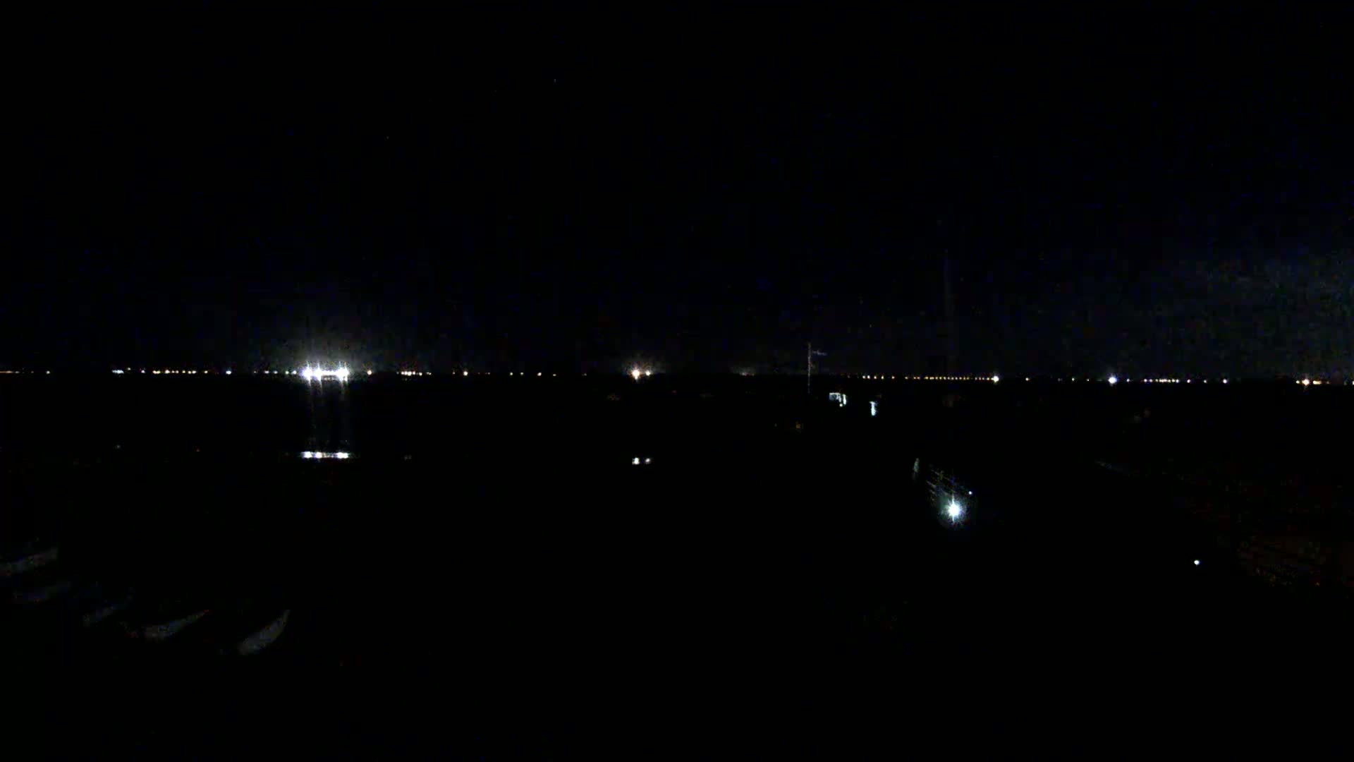 A dark, nighttime scene shows a distant line of lights possibly from a city or town, with a few scattered lights closer to the viewer's perspective in the foreground.