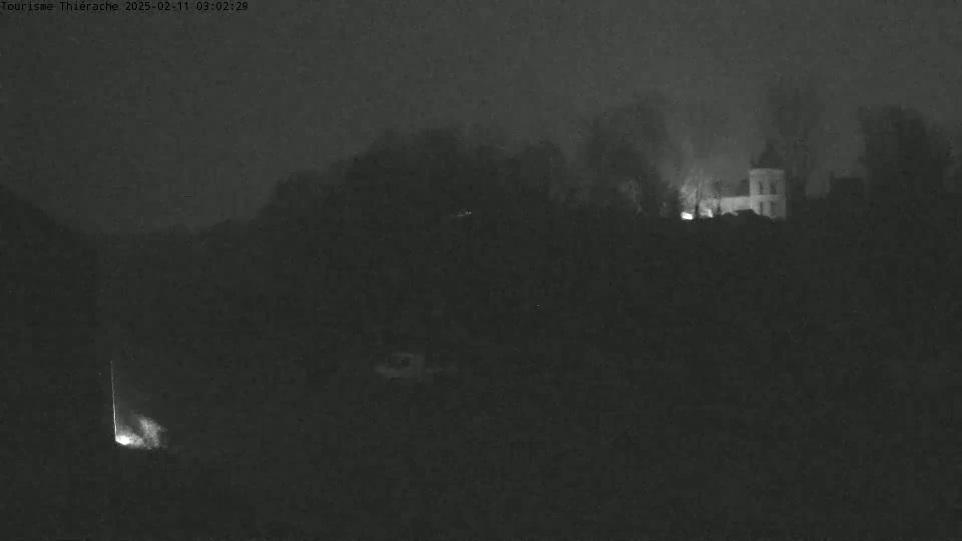 A dimly lit, foggy nighttime scene shows a building atop a hill with a few faint lights visible.