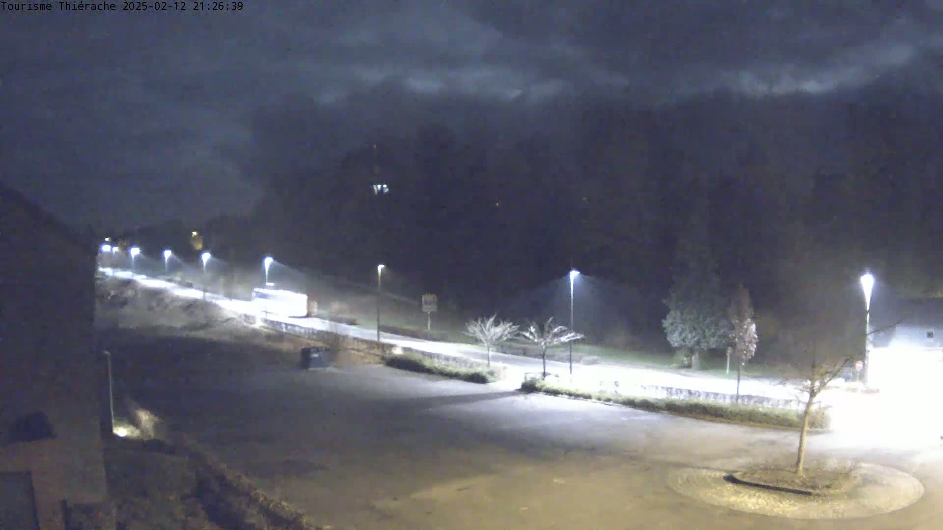 A nighttime, dimly lit road with several vehicles visible, under a cloudy sky.