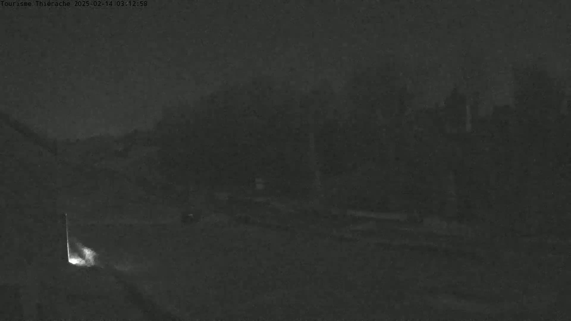 A nighttime, low-light image shows a dark road leading into a dark, tree-lined area.