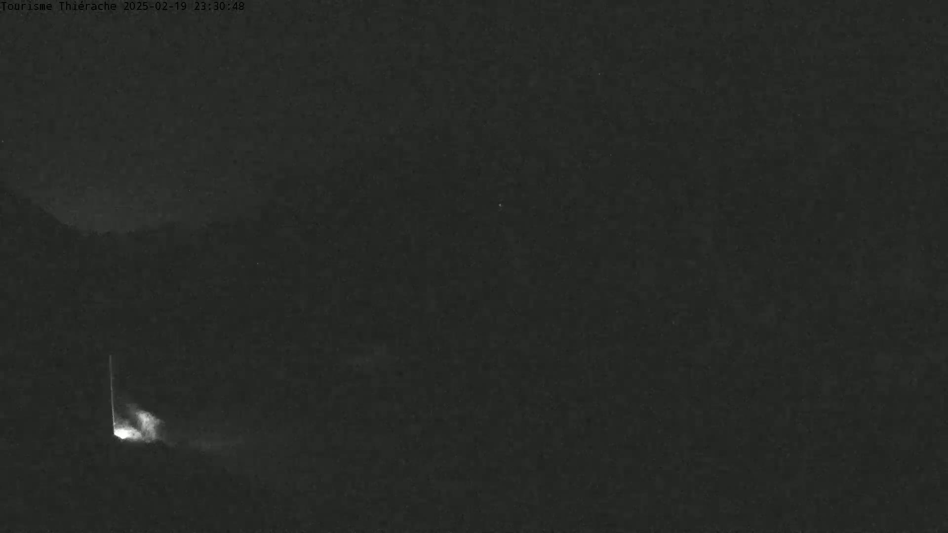 A nighttime, dark scene shows a faint, vertical light source at the bottom left, possibly a light or a reflection, against a mostly dark background.
