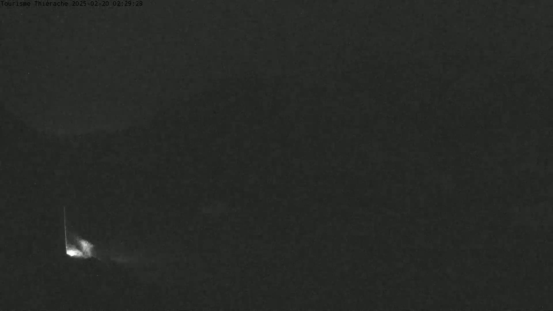 A faint, bright light is visible at the bottom left of a dark, nighttime scene.