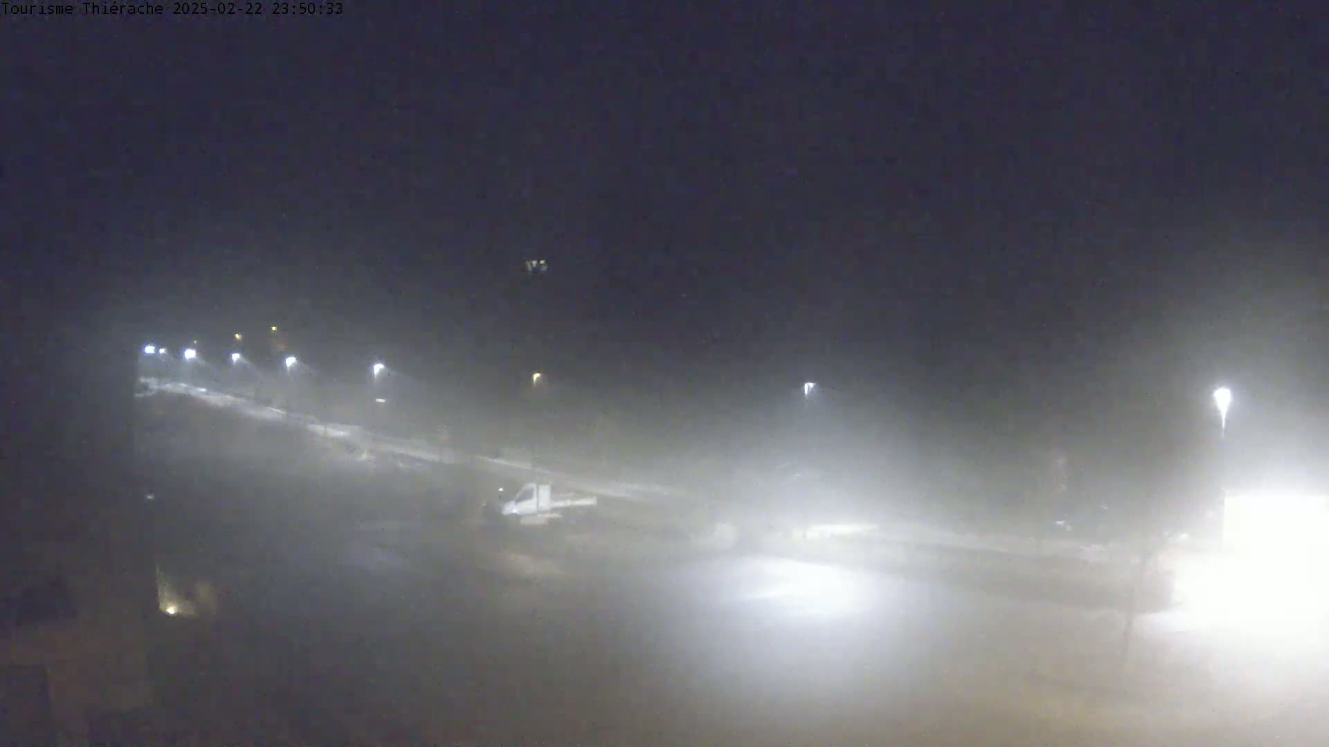 A foggy night scene shows a road with dimly lit streetlights and a vehicle partially obscured by the fog.
