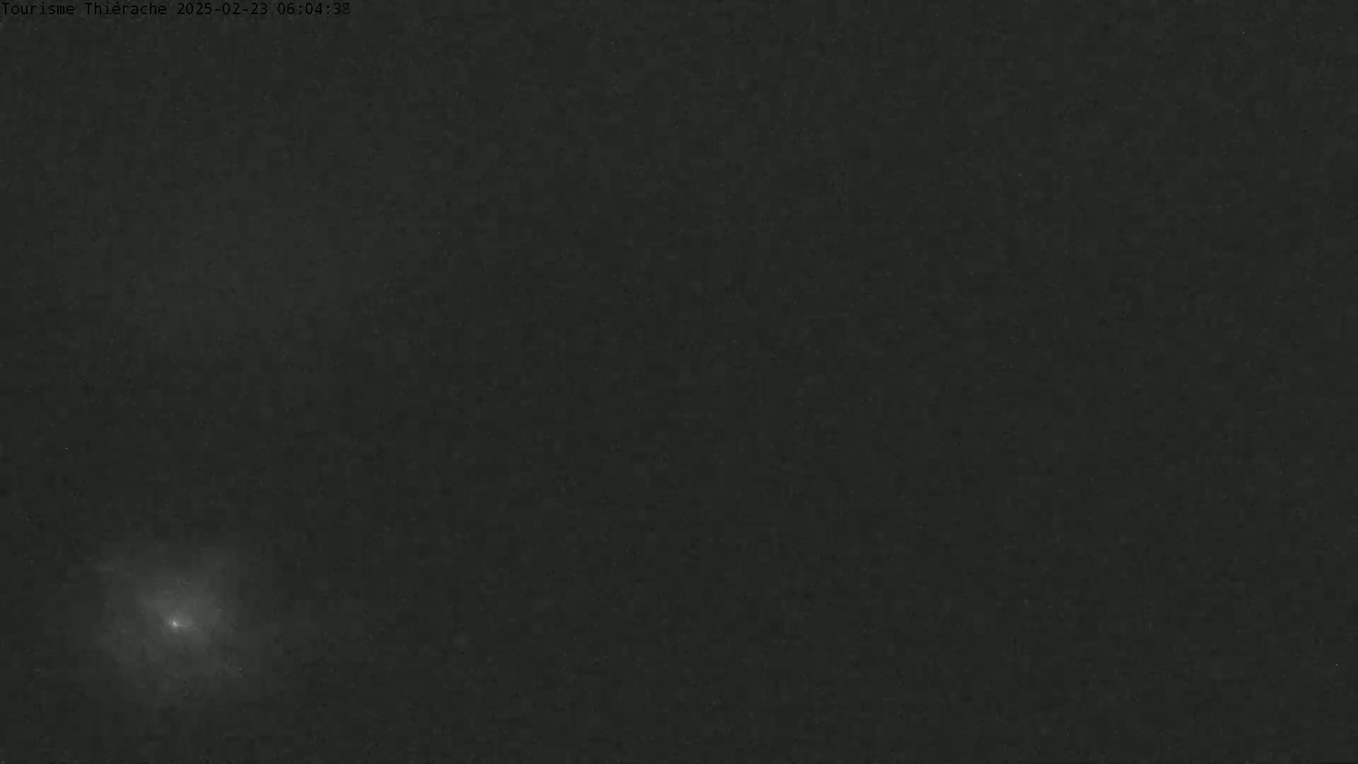 A low-light image shows a bright, blurry object in the lower-left corner against a dark, mostly featureless background.