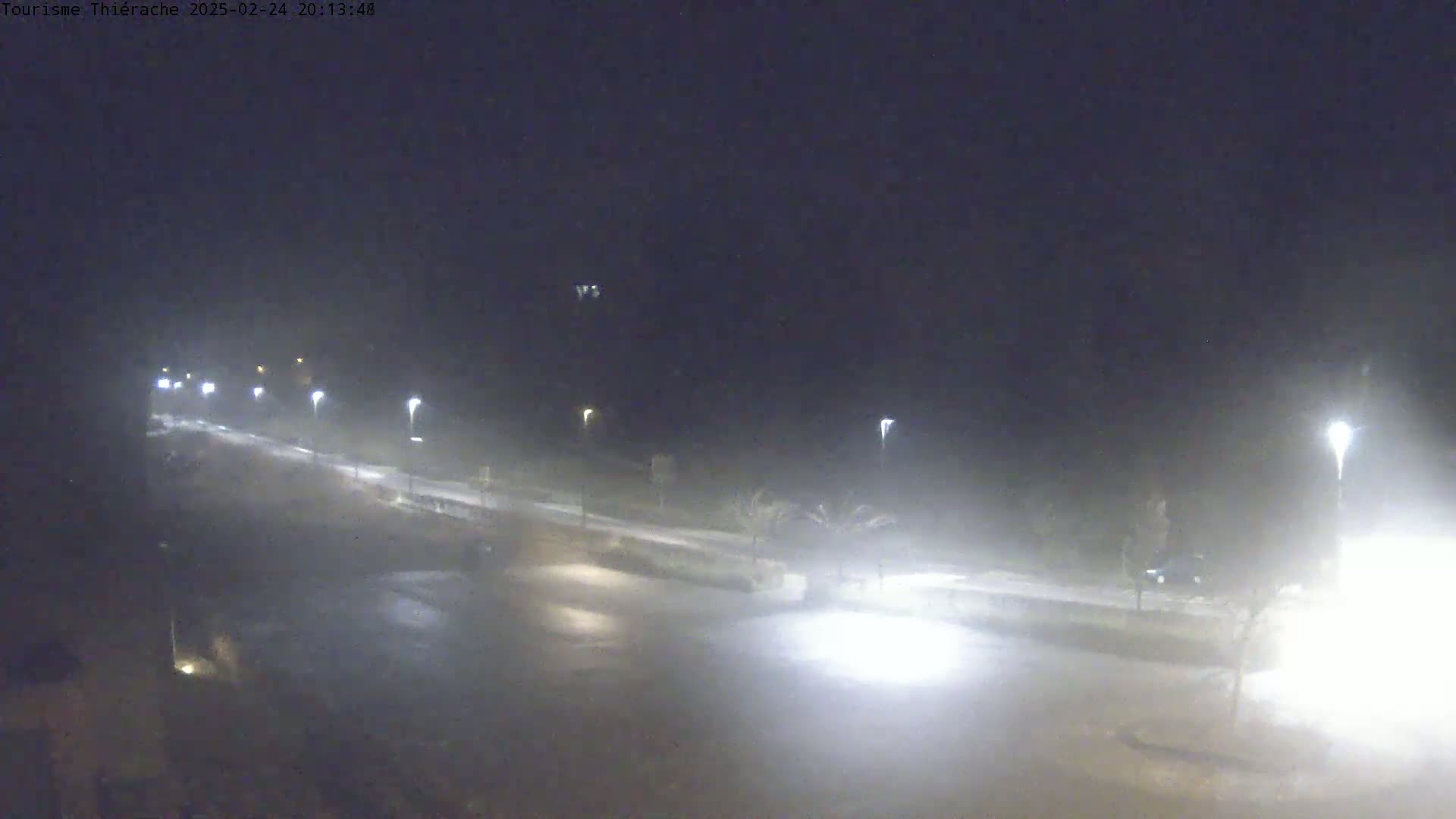 A nighttime, hazy view of a paved road with streetlights and sparse vegetation, possibly a parking lot, is visible.