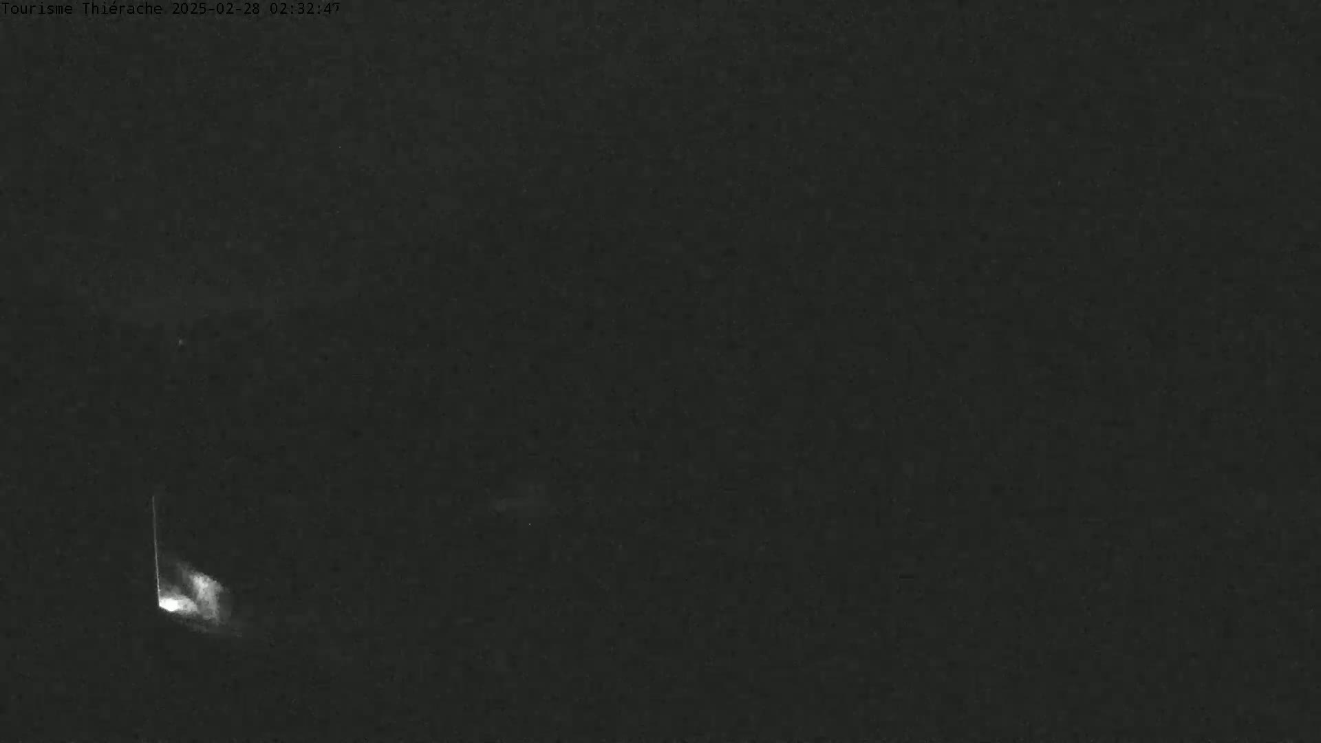 A low-light, nighttime image shows a faint, vertical streak of light in the bottom left corner of an otherwise dark scene.