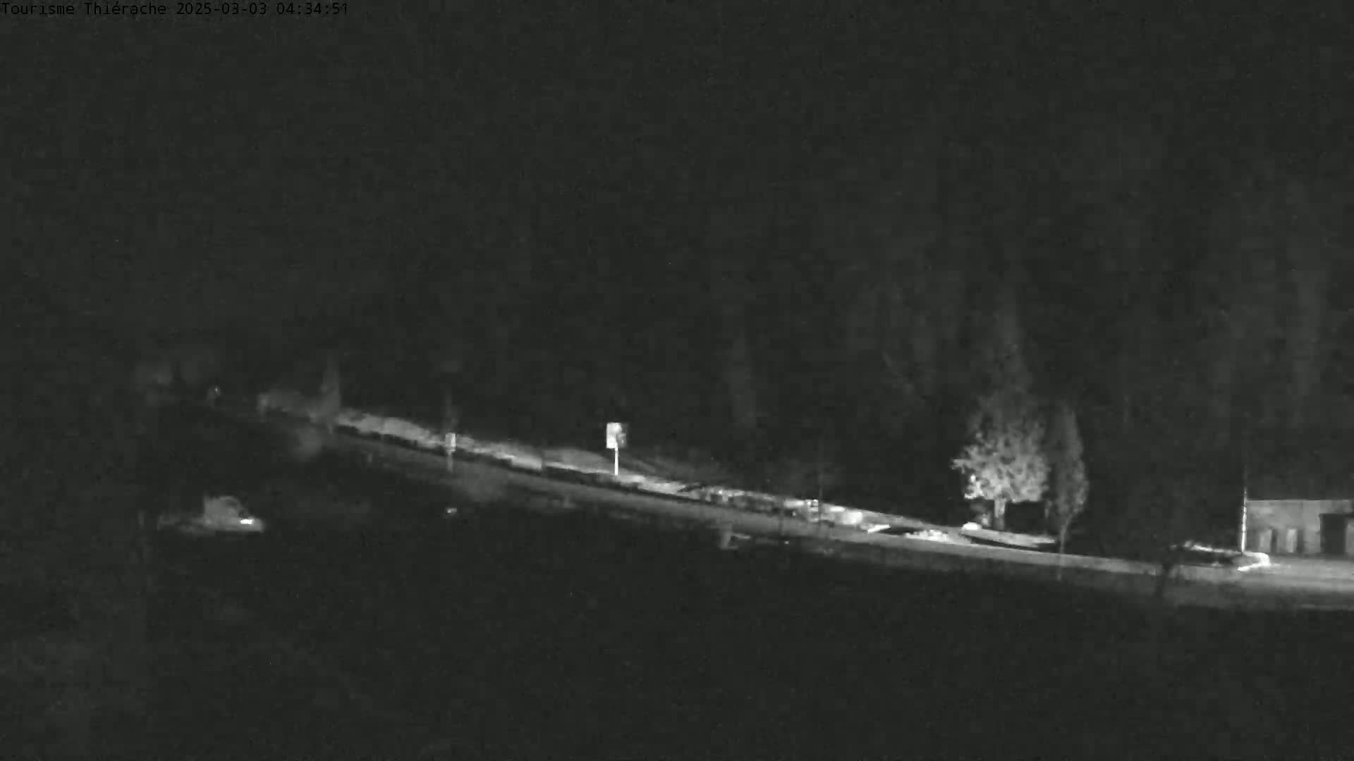 A nighttime, low-light image shows a road curving gently downward, lined with dark trees and a few indistinct vehicles.