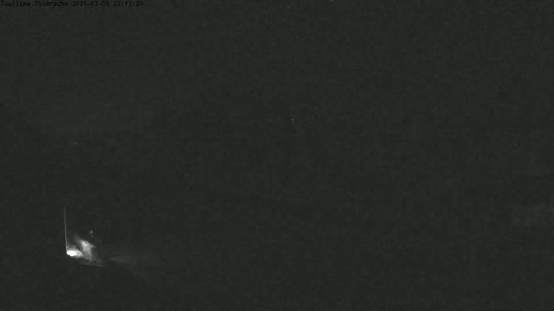 A low-light, nighttime image shows a faint, bright vertical line in the lower left corner, possibly a light source, against a mostly dark background.