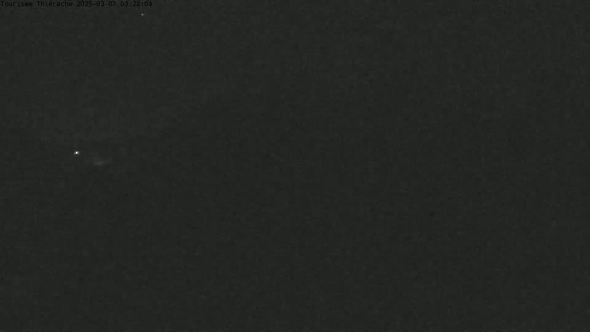 A dark, nighttime scene shows a faint light in the distance under a clear sky.