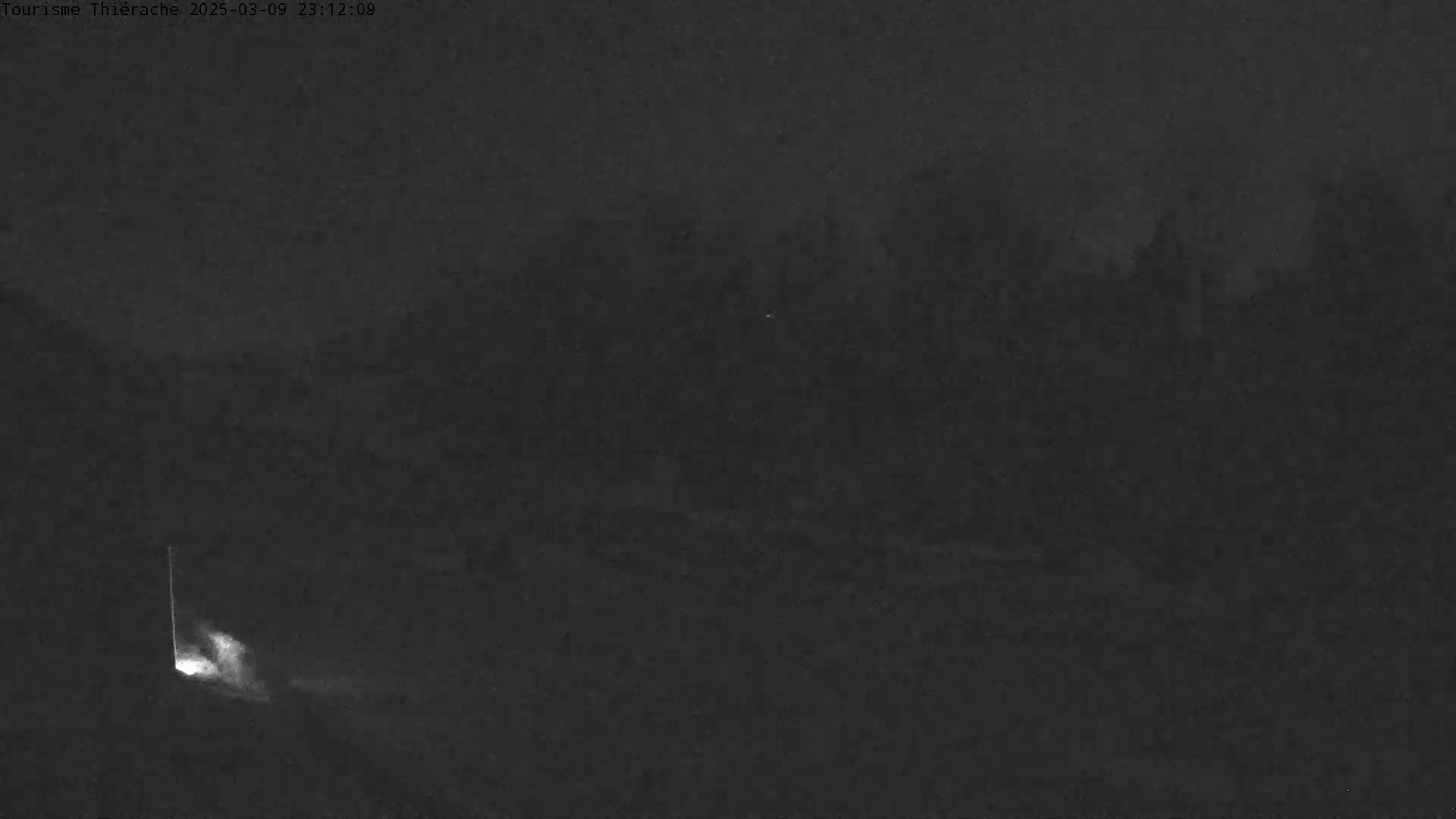 A nighttime, low-light image shows a dimly lit area with a faint light source in the lower left corner and a dark, indistinct background.