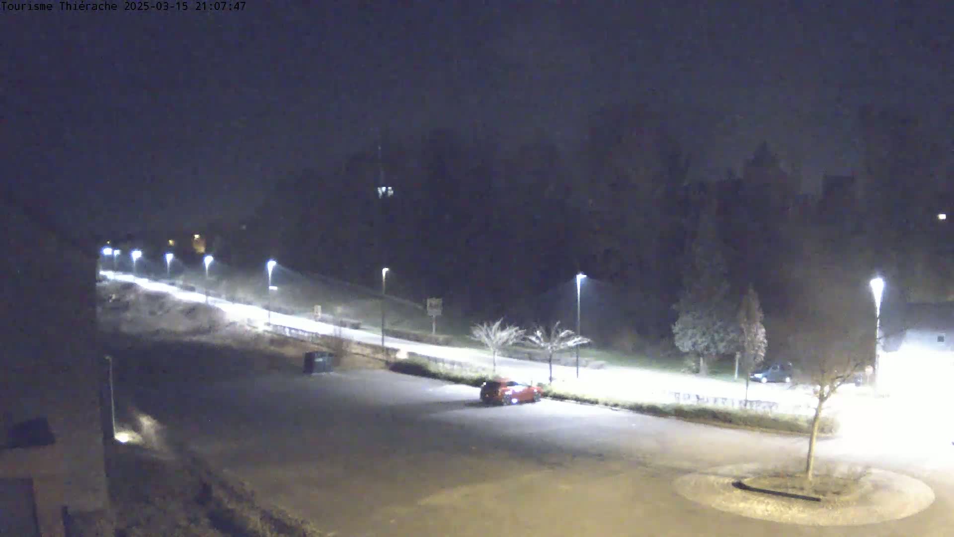 A nighttime view of a mostly empty parking lot next to a road lined with streetlights, under hazy or foggy conditions.