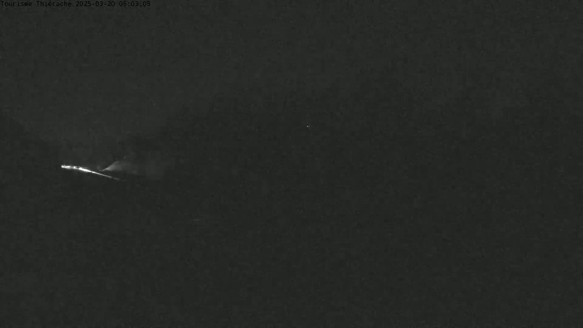 A low-light nighttime image shows a single set of headlights moving across the bottom of the frame.