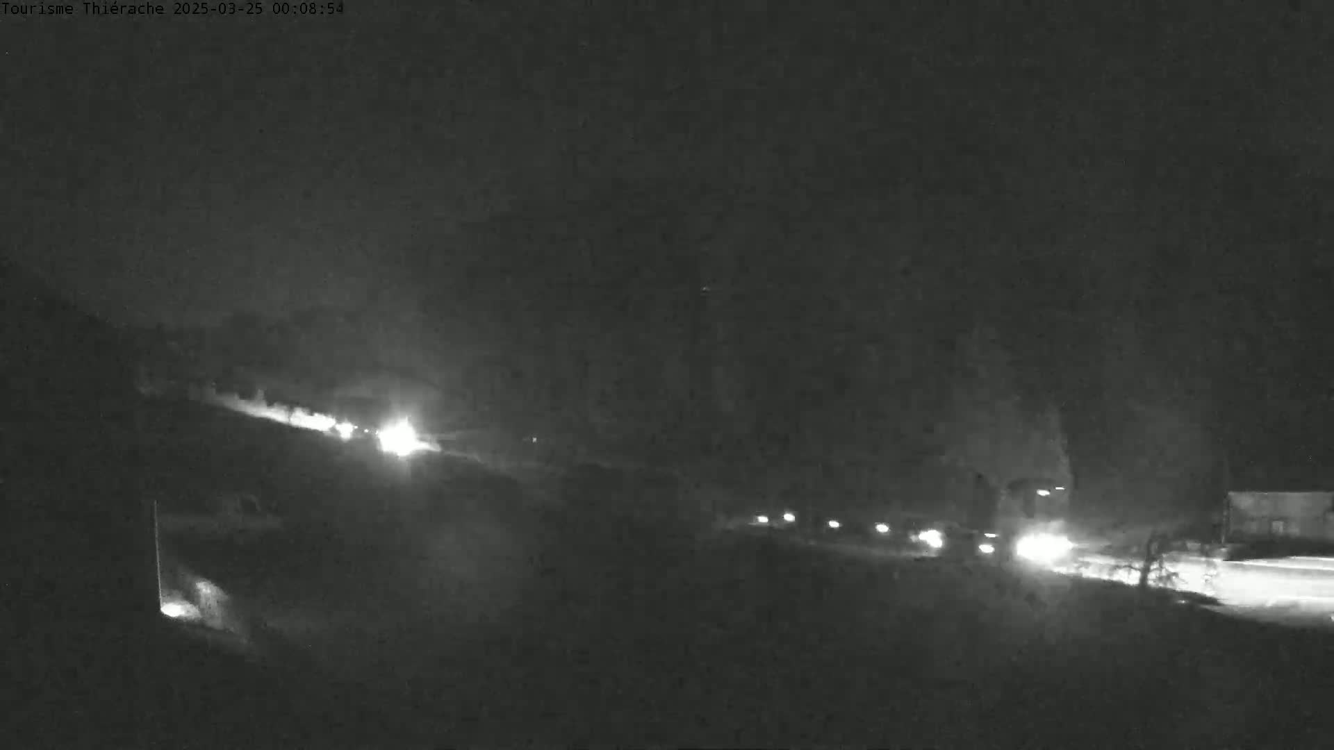 A nighttime, low-light image shows a road with several vehicles traveling along it, under a dark sky.