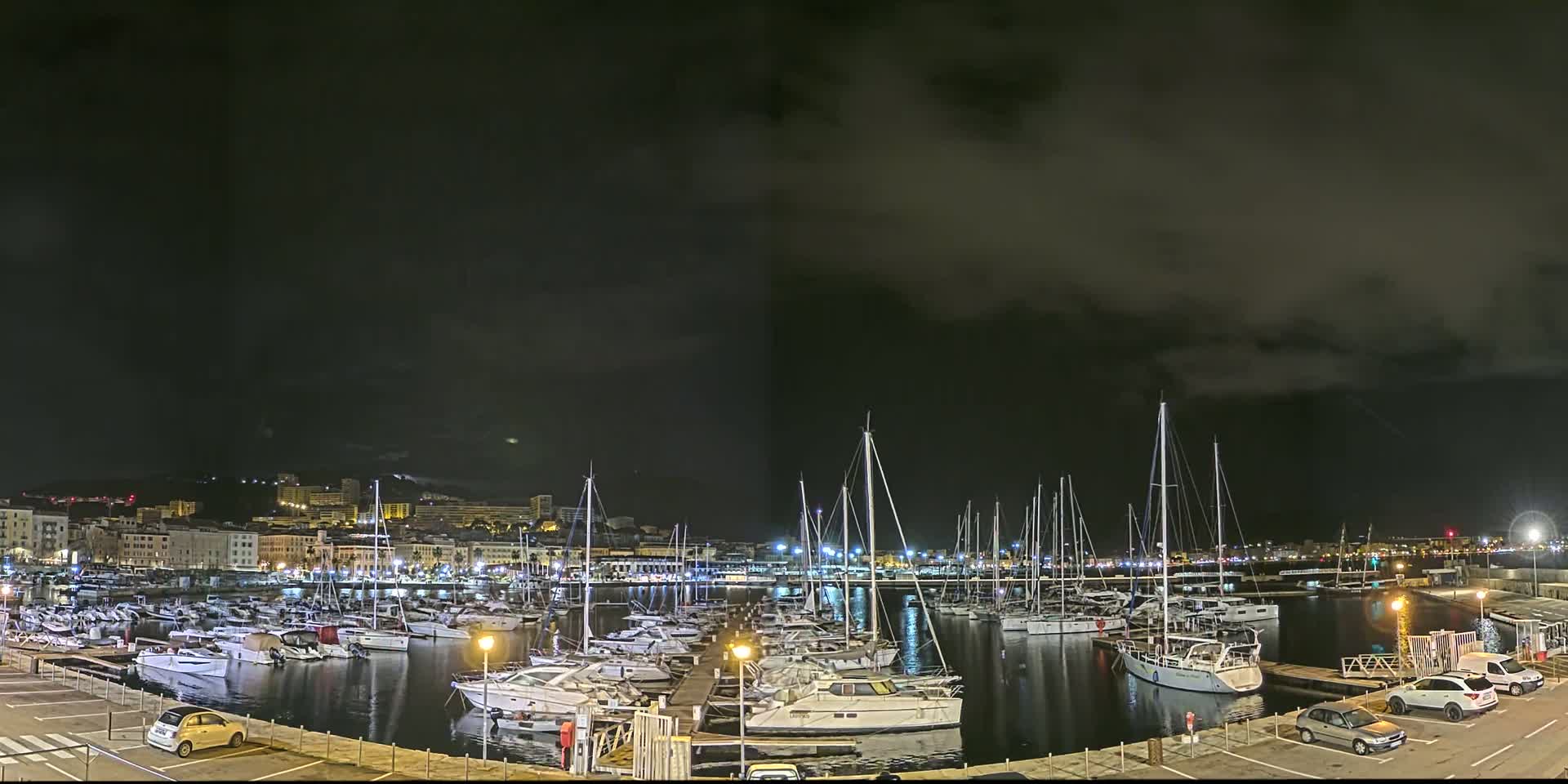 A nighttime view of a marina filled with docked boats under a dark, cloudy sky.