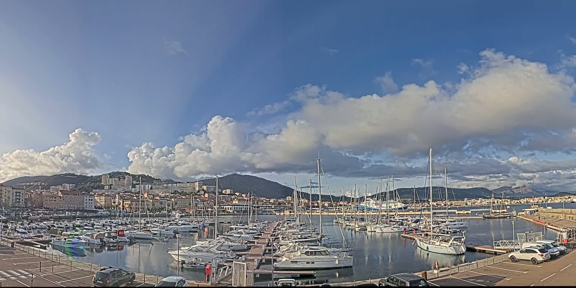A marina filled with numerous boats is nestled next to a city under a partly cloudy sky.