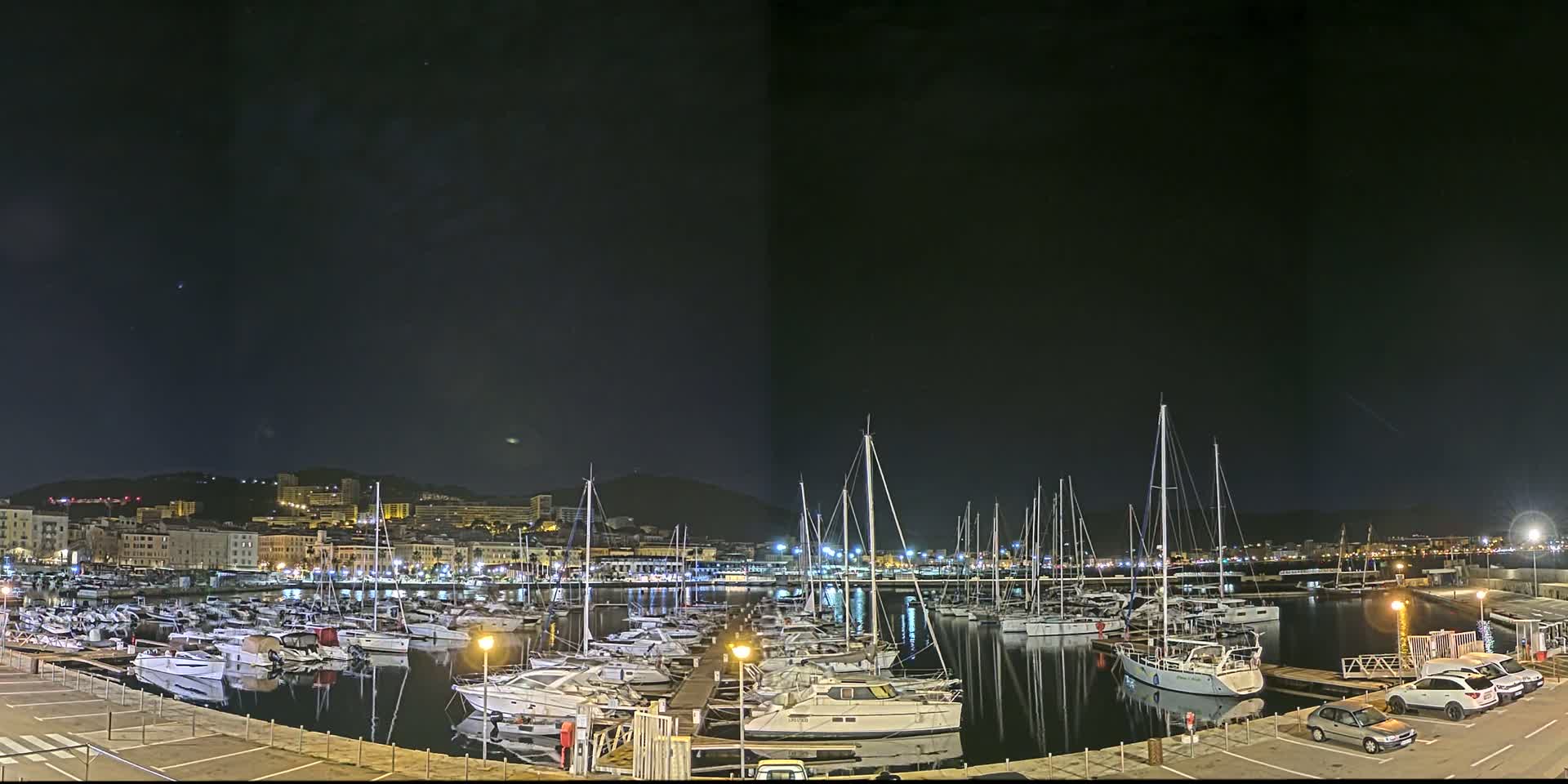A marina filled with numerous boats is illuminated at night under a dark sky.