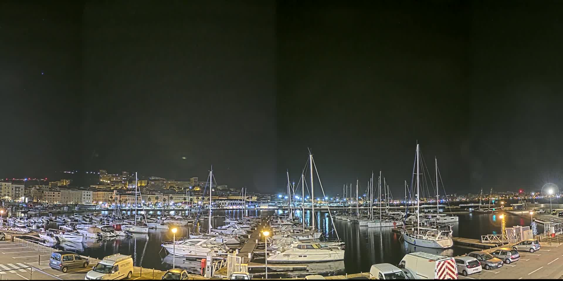 A marina filled with numerous boats is illuminated at night under a clear, dark sky.