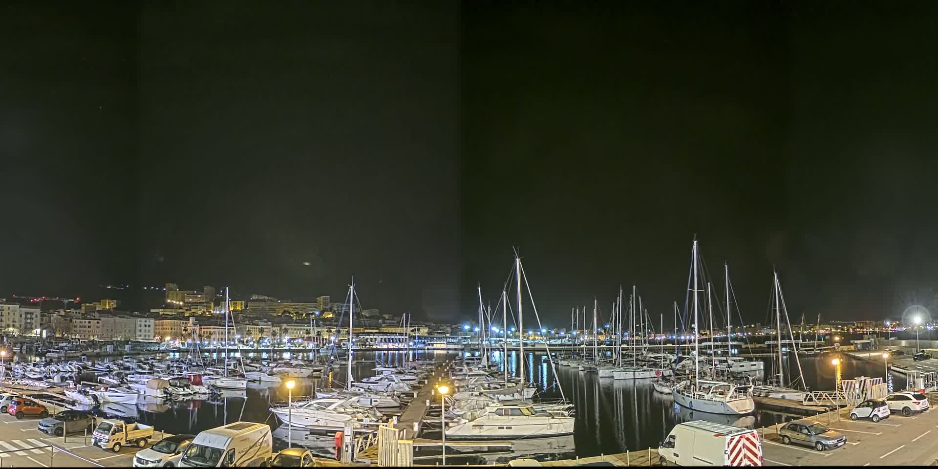 A marina filled with sailboats and motorboats is illuminated at night under a dark sky.