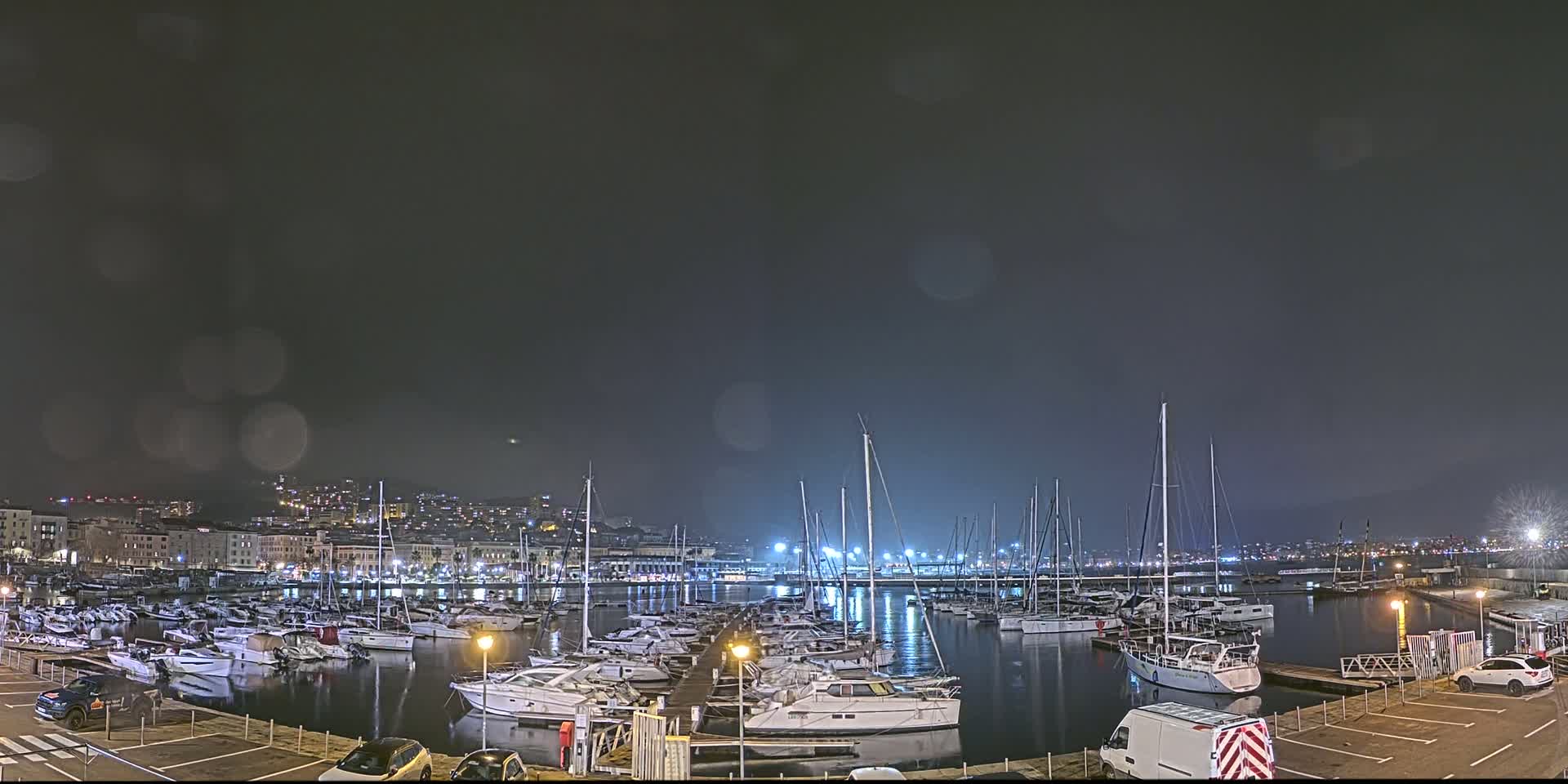 A marina filled with numerous boats is seen at night under a dark, possibly overcast sky.