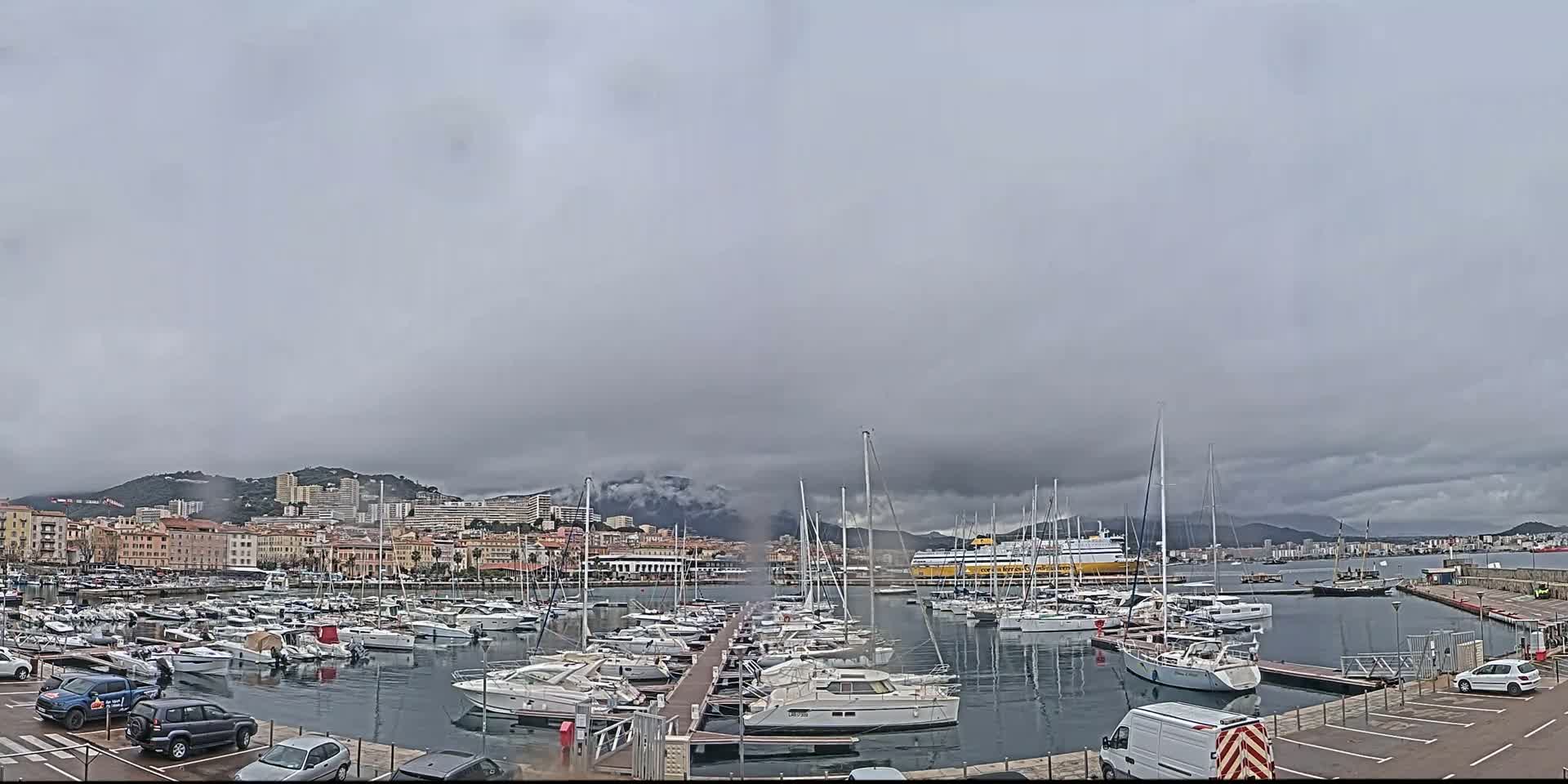 A harbor filled with many boats and yachts is situated near a city under an overcast sky.