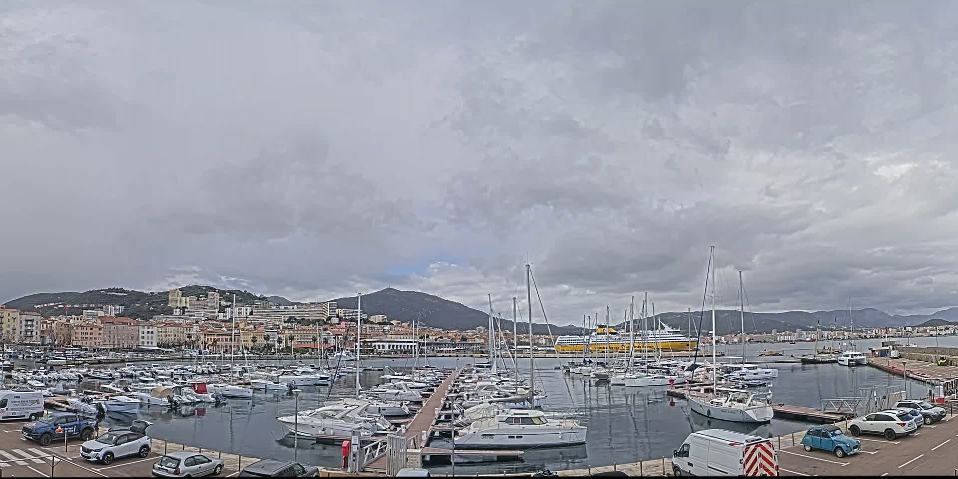 A harbor filled with sailboats and yachts is situated in front of a city under a cloudy sky.