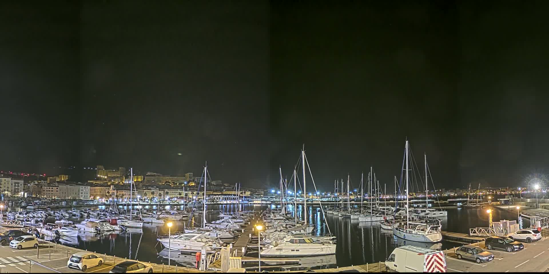 A marina filled with numerous boats is illuminated at night under a dark, clear sky.