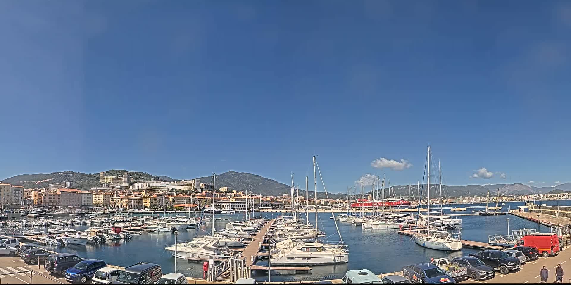 A harbor filled with numerous sailboats and motorboats is situated in front of a city under a clear blue sky.