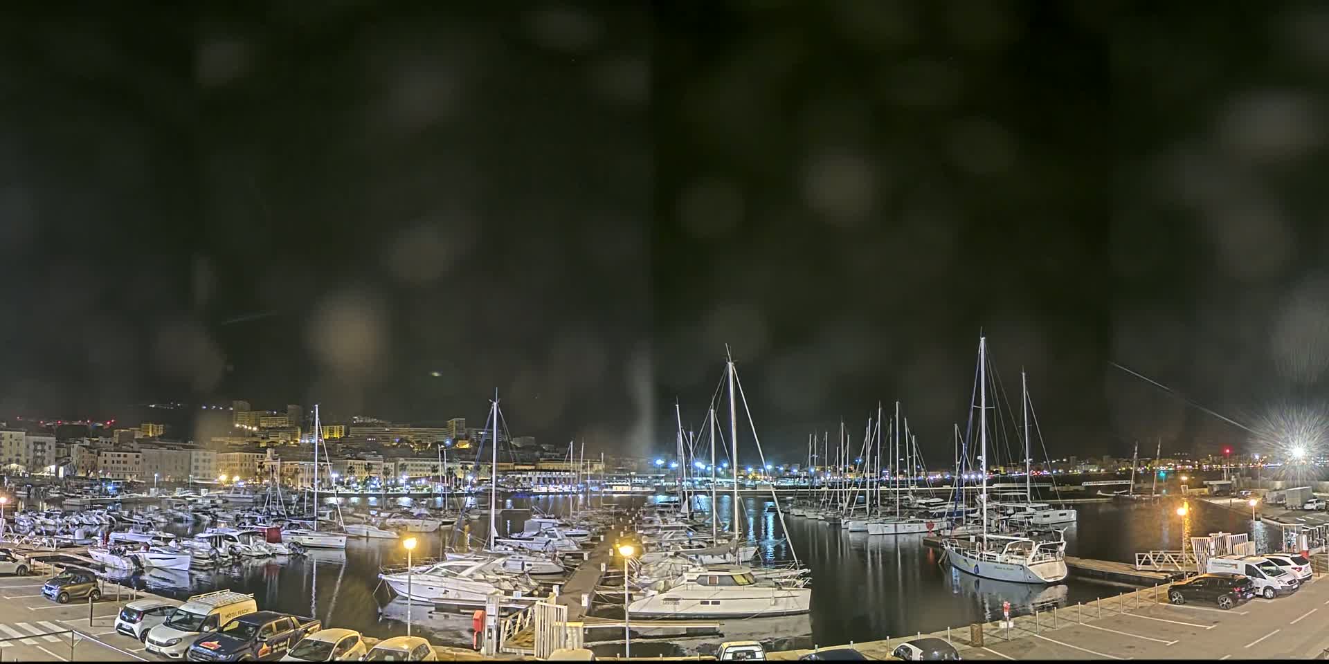 A nighttime view of a harbor filled with numerous boats and yachts under a dark, slightly hazy sky.