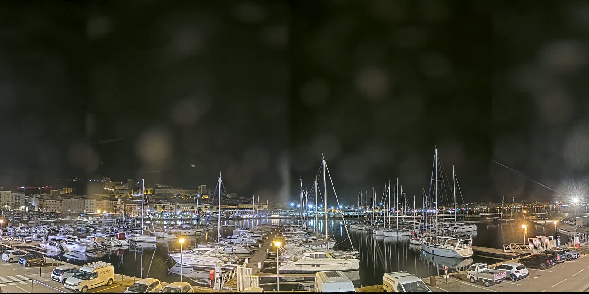 A marina filled with numerous boats is seen at night under a dark, slightly hazy sky.