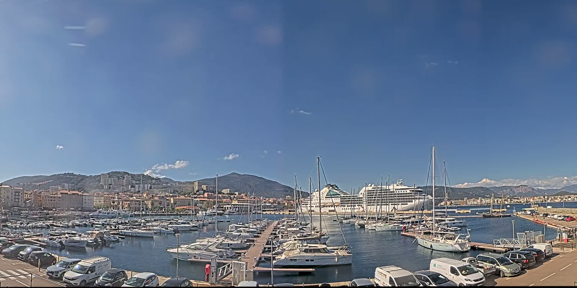 A large cruise ship is docked in a harbor filled with numerous yachts and sailboats, under a clear blue sky.