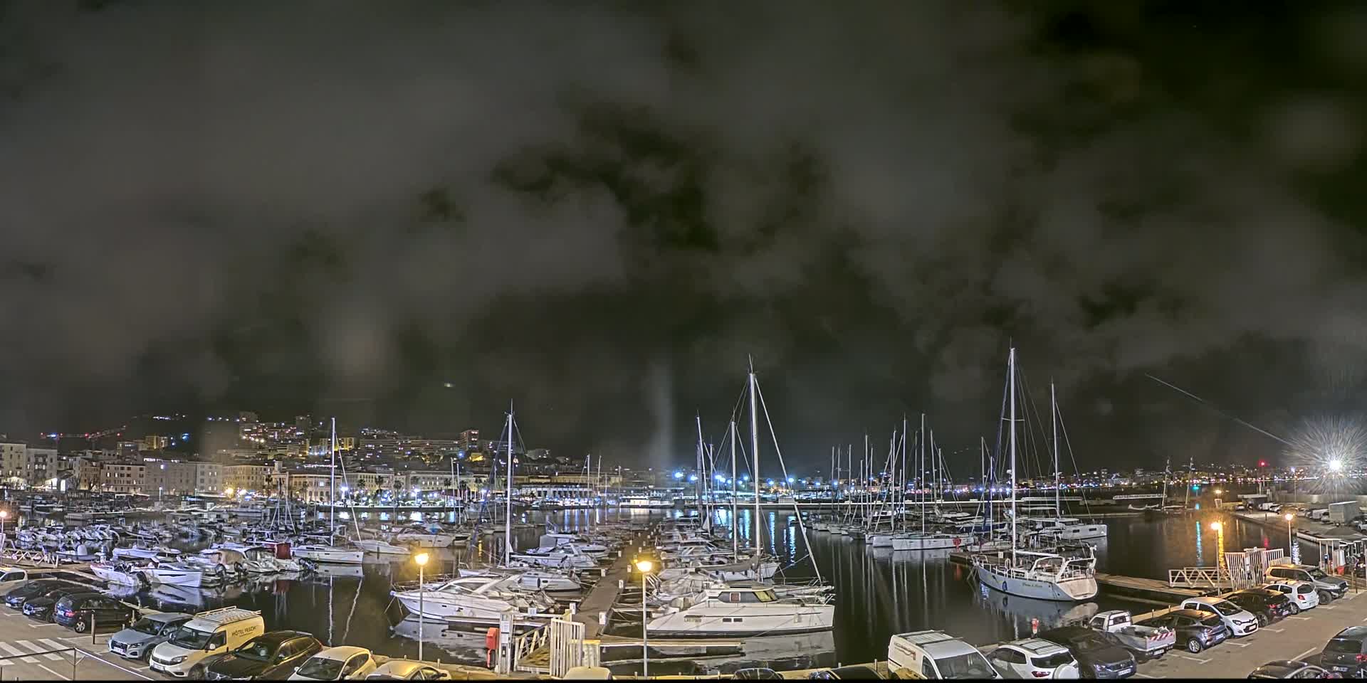 A nighttime harbor filled with numerous boats under a dark, cloudy sky.