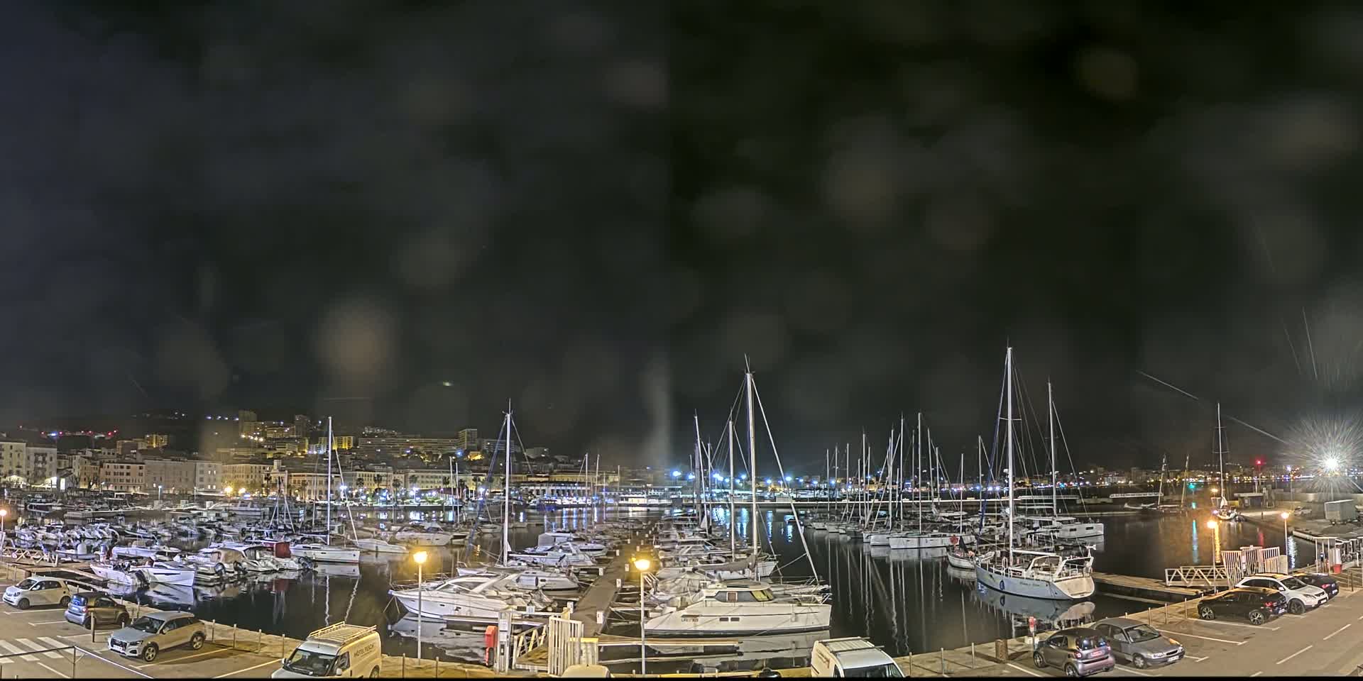 A nighttime view of a marina filled with numerous boats under a dark, possibly rainy sky.