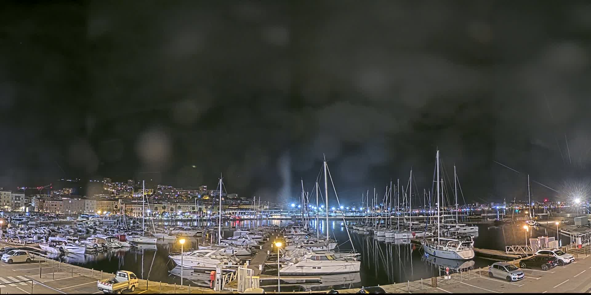 A nighttime view of a marina filled with boats under a dark, cloudy sky.