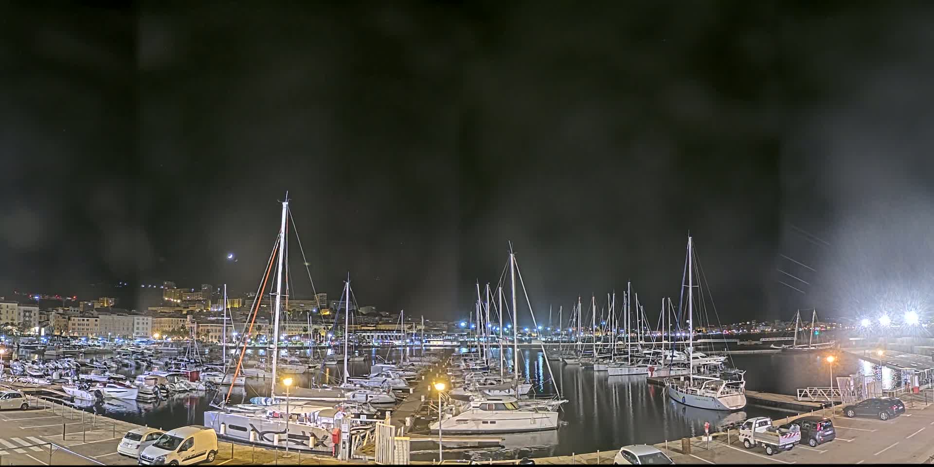 A nighttime marina filled with sailboats and motorboats under a dark, slightly hazy sky.