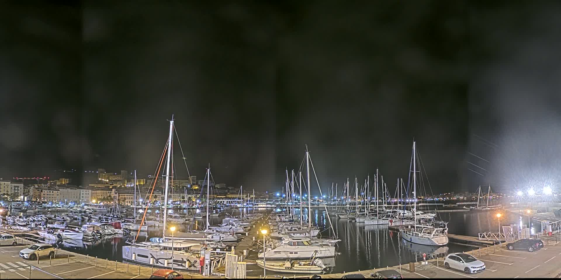 A nighttime view of a marina filled with sailboats and motorboats under a dark, cloudy sky.