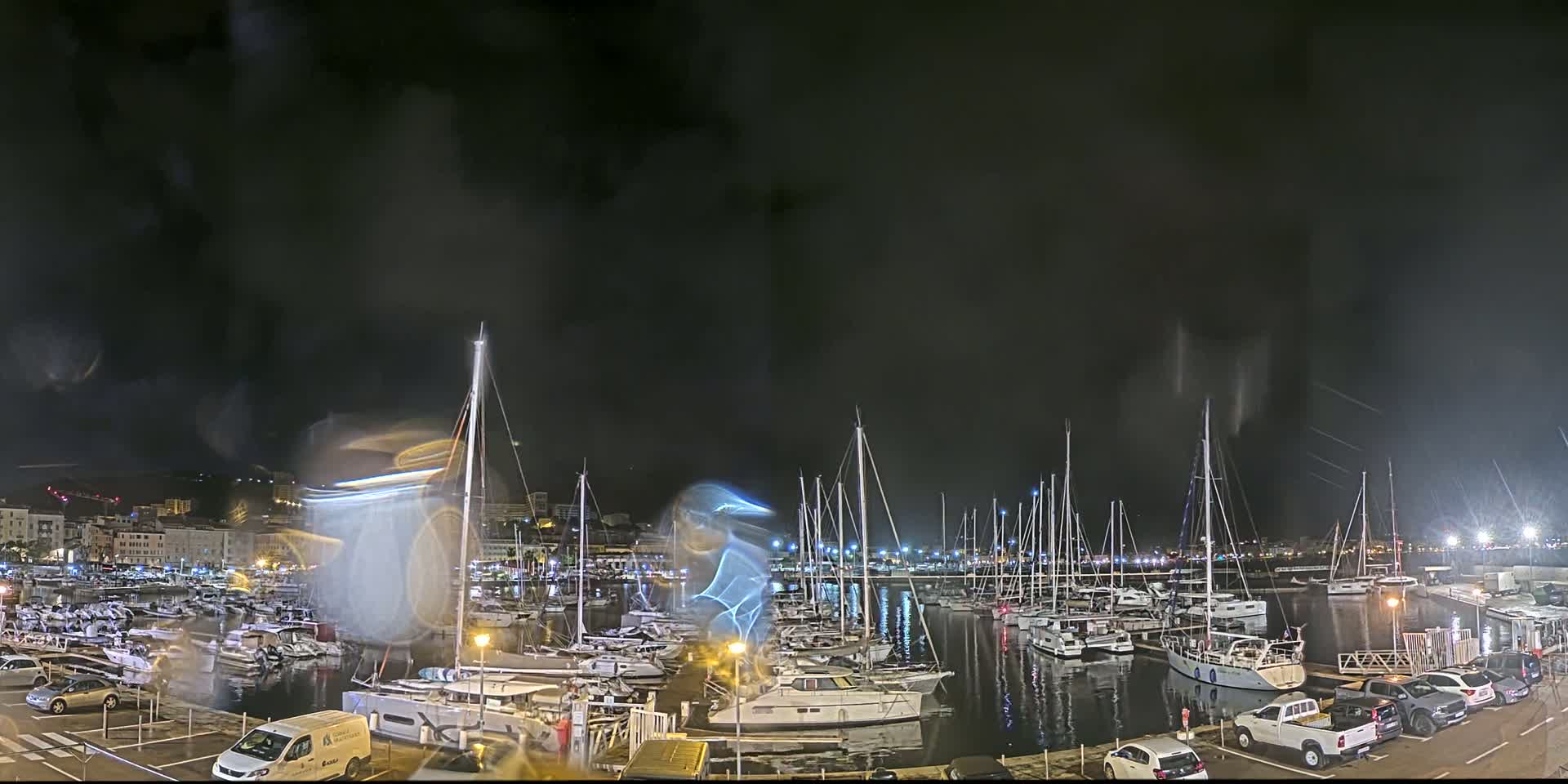 A nighttime marina filled with sailboats and motorboats under a dark, possibly rainy sky.