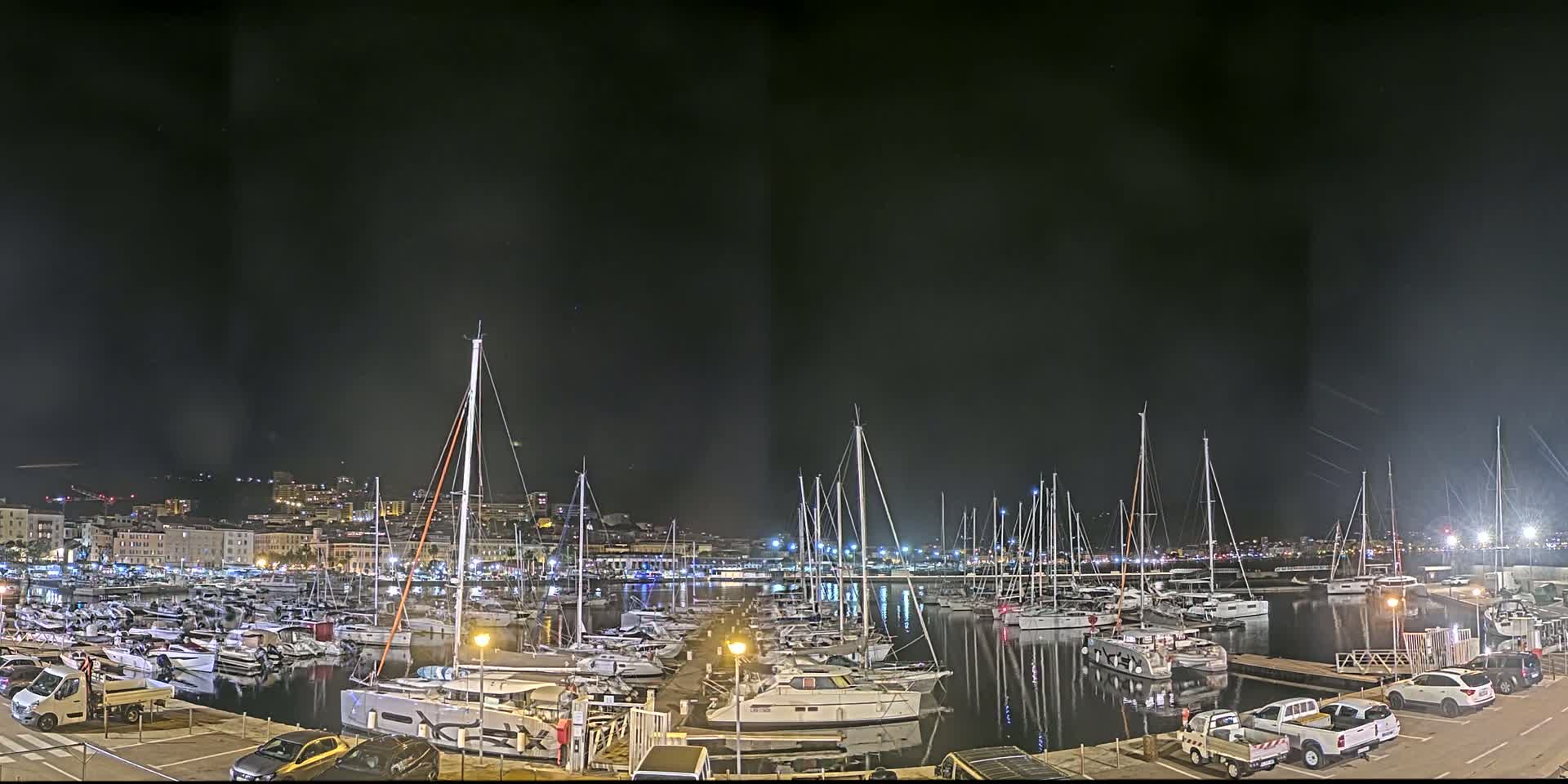 A marina filled with numerous boats and yachts at night, under a dark, possibly slightly hazy sky.