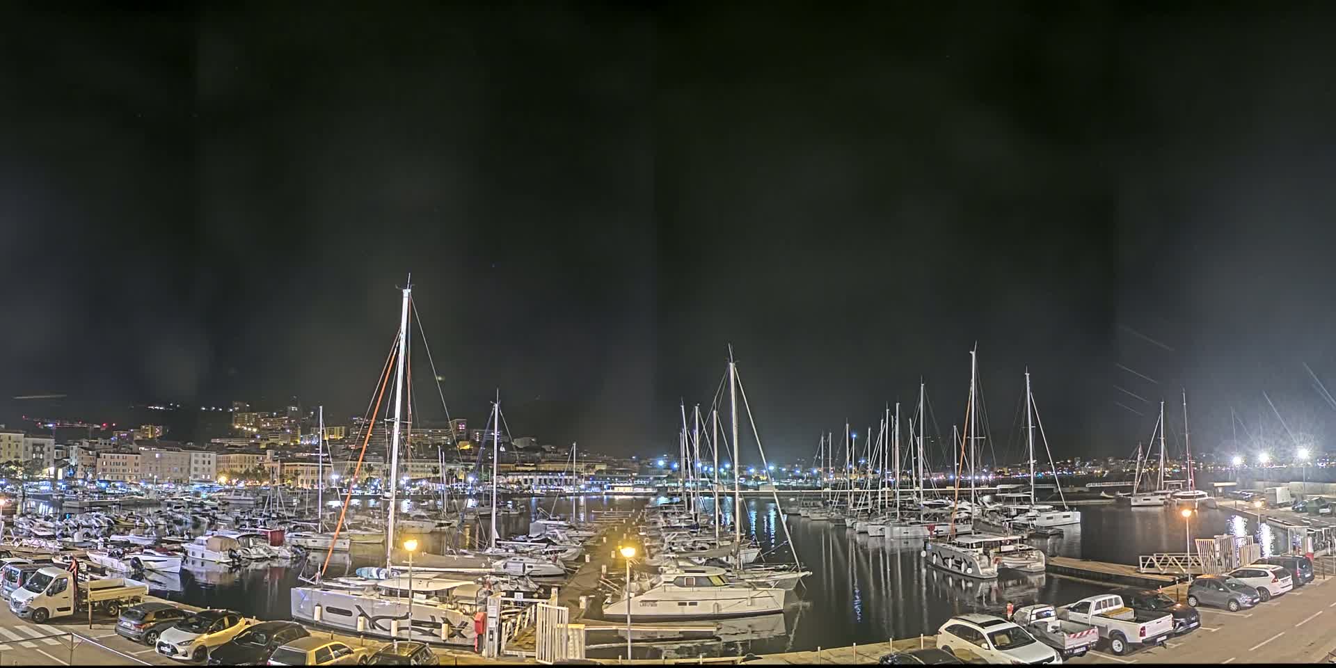 A marina filled with numerous sailboats and yachts is illuminated at night under a dark sky.