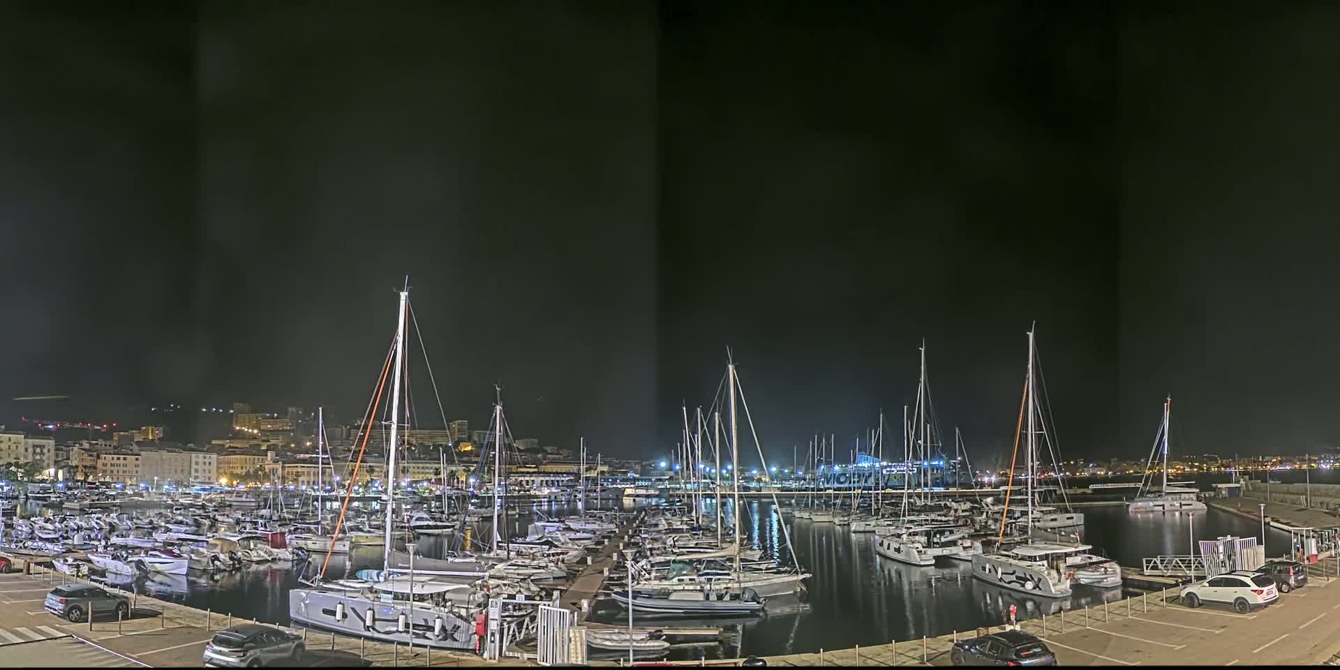 A marina filled with sailboats and motorboats is illuminated at night under a dark sky.