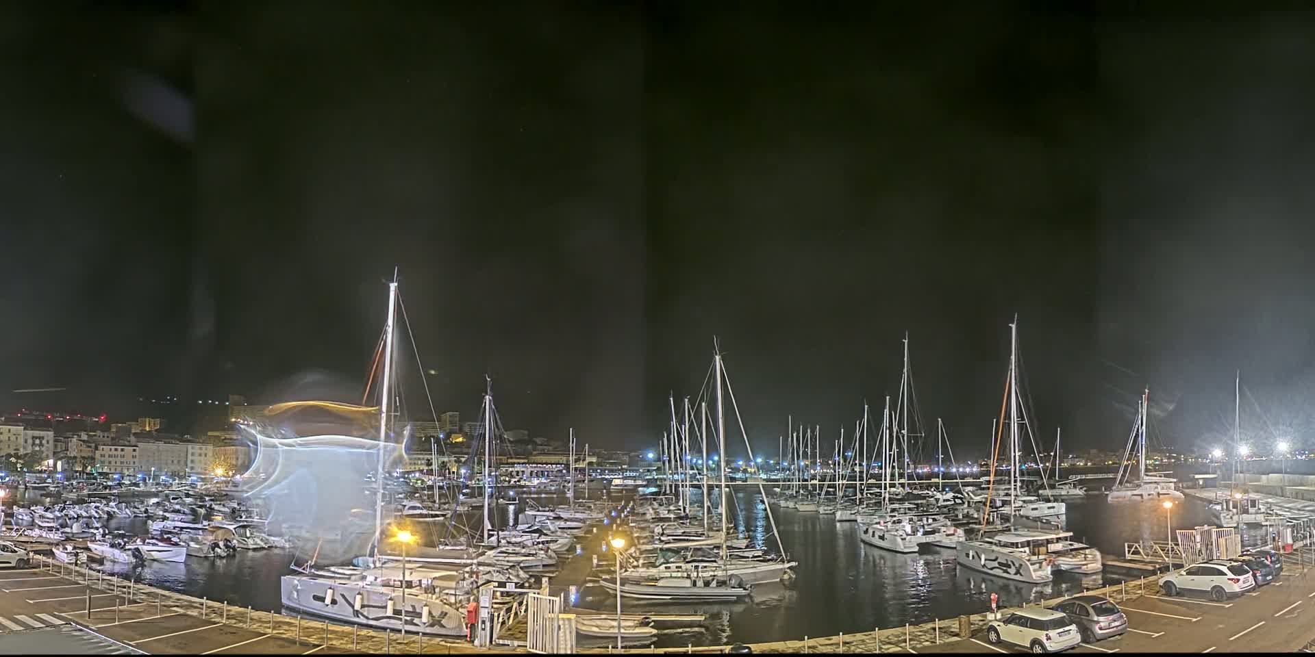 A nighttime view of a marina filled with sailboats and yachts under a dark, slightly hazy sky.
