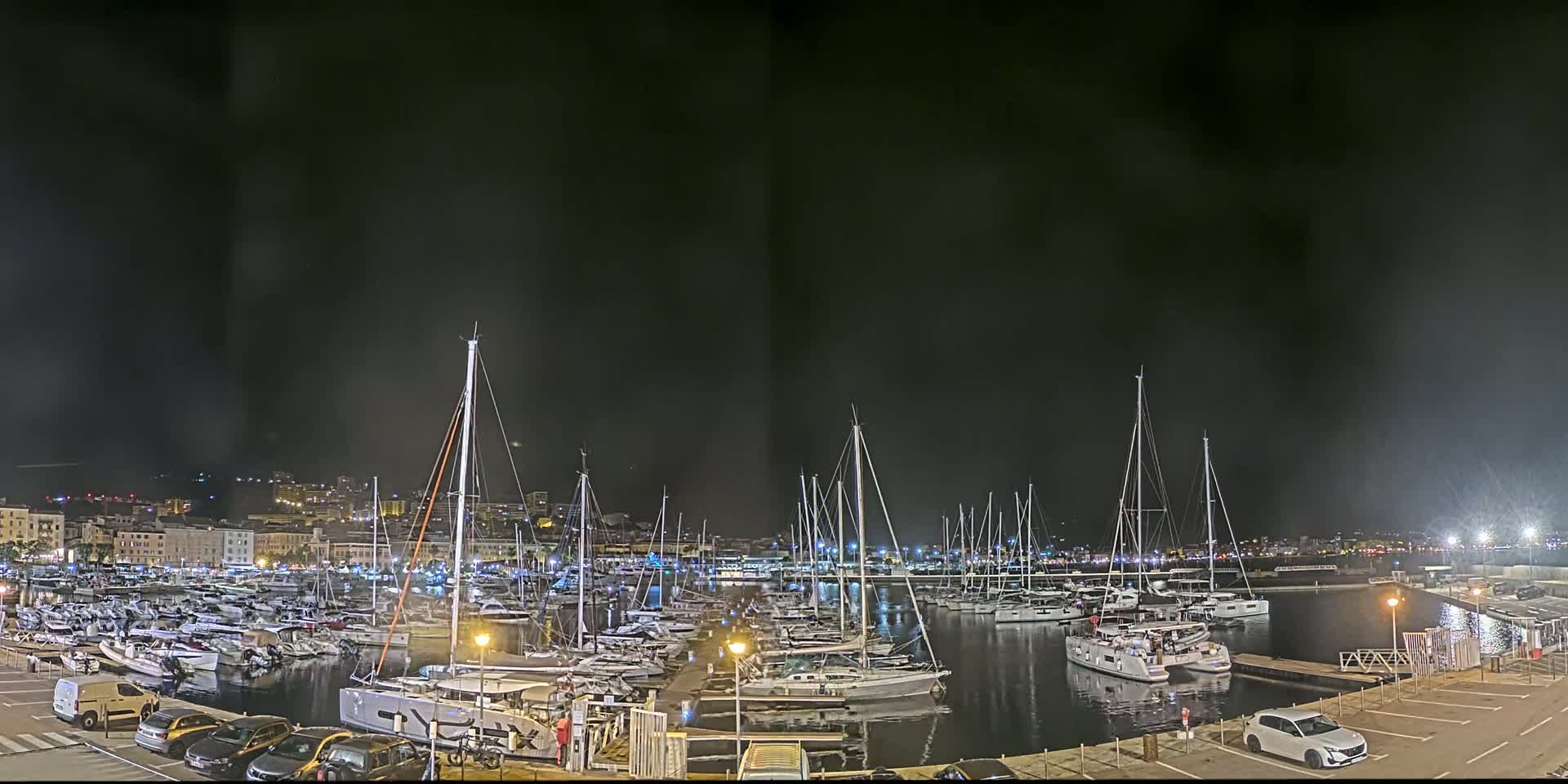 A marina filled with numerous sailboats and yachts is seen at night under a dark, cloudy sky.