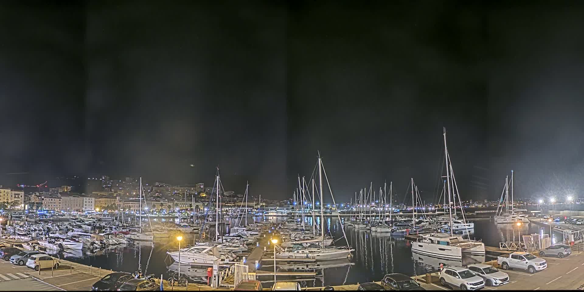 A nighttime view of a marina filled with numerous boats and yachts, under a dark, slightly hazy sky.