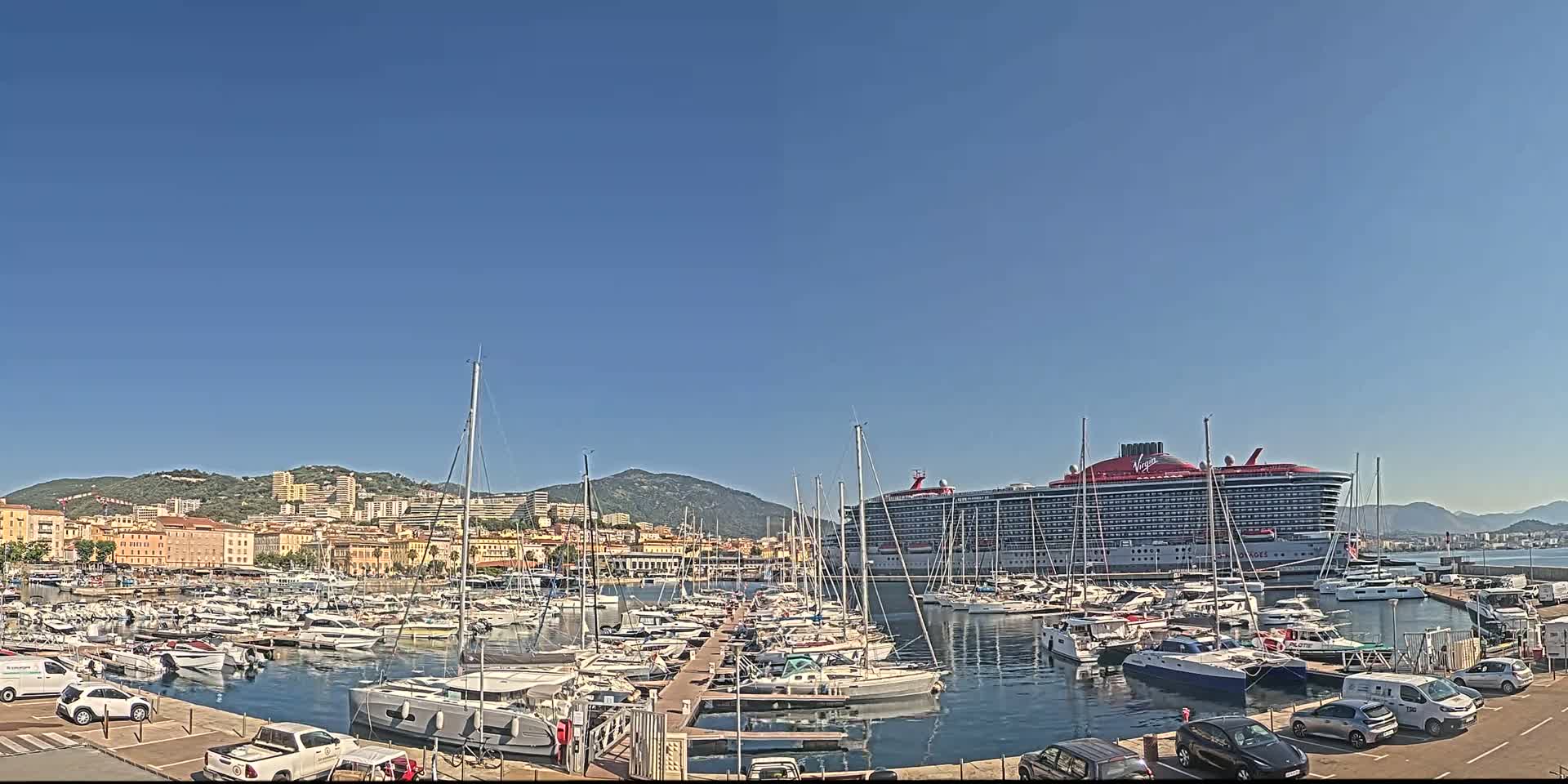 A large cruise ship is docked in a harbor filled with numerous smaller boats, under a clear blue sky.