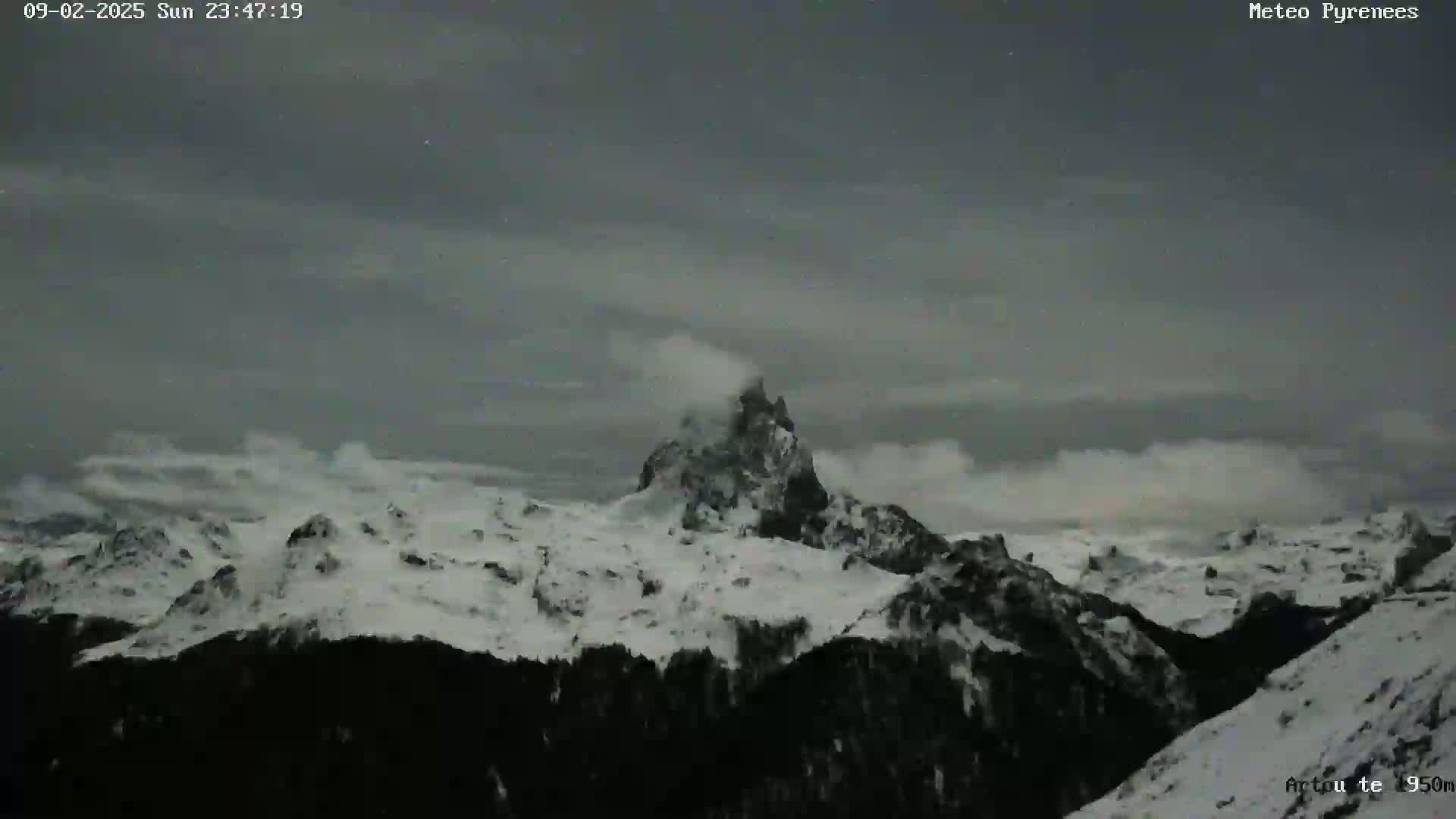 A snow-covered mountain range is visible under a dark, cloudy night sky.