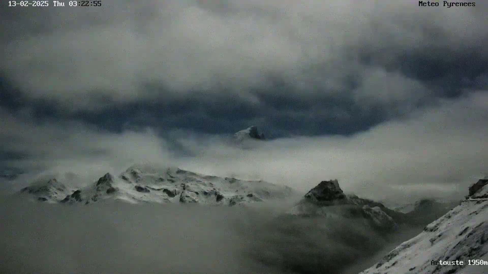 Snow-covered mountains are partially obscured by a thick layer of fog or low clouds under a dark, overcast sky.