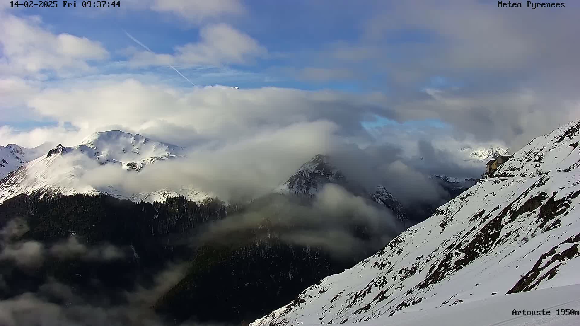 Snow-covered mountains are partially obscured by clouds under a partly sunny sky.