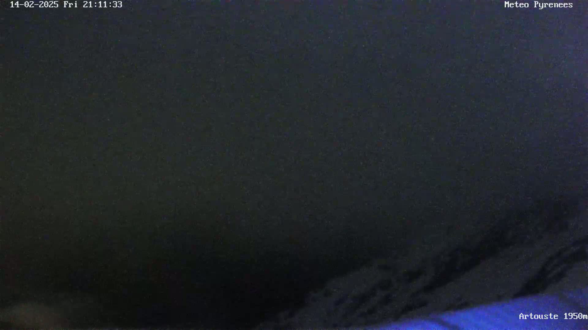 A dark, nighttime view shows a low-lying area of dark blue and black, possibly snow-covered ground or mountains, under a dark, possibly cloudy sky.